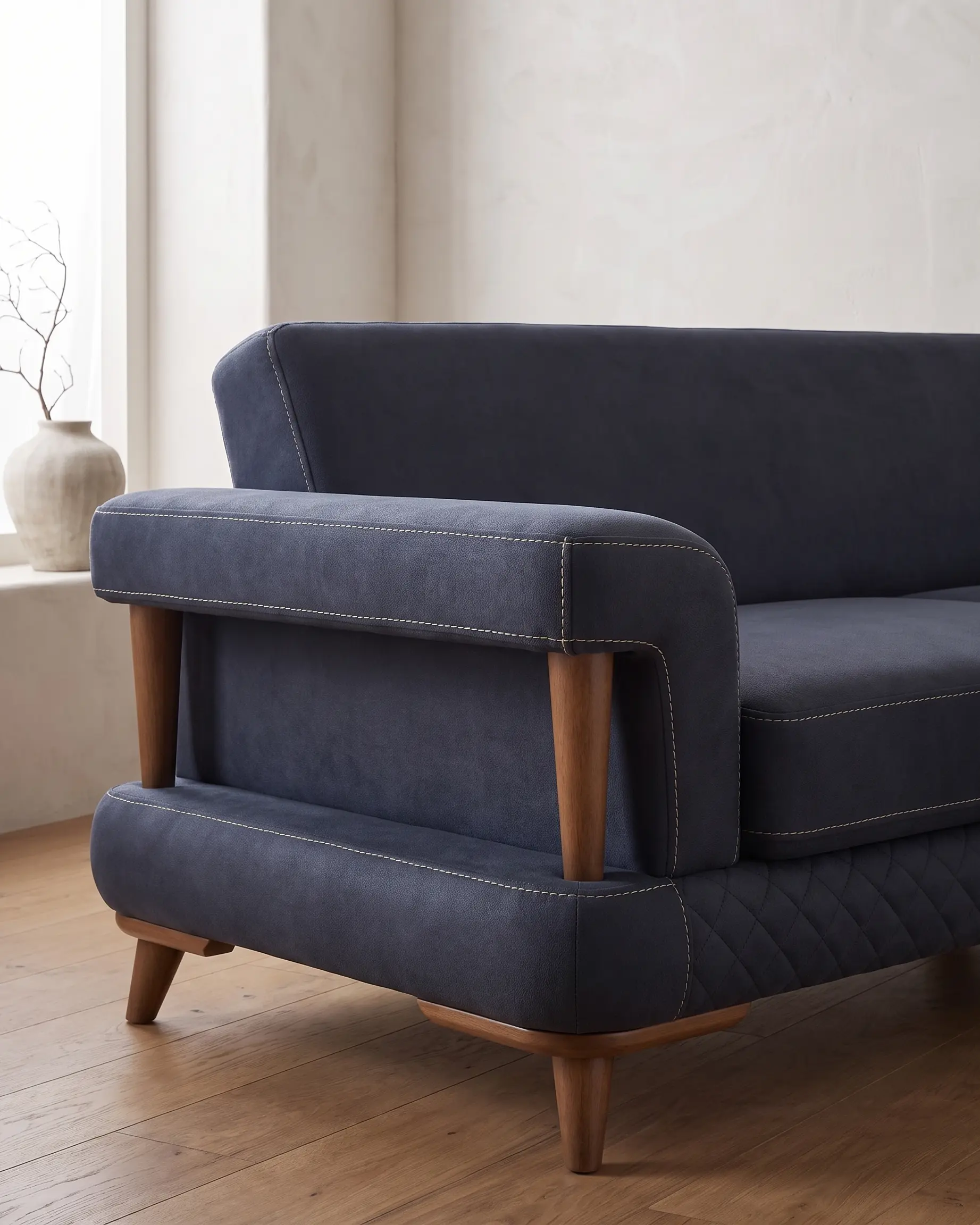 Aurigo sofa, krupni plan jednog kraja: dva drvena stuba drže rukonaslon, pregrada u istoj tkanini zatvara otvor, a drvena letvica obilazi ugao pod postoljem