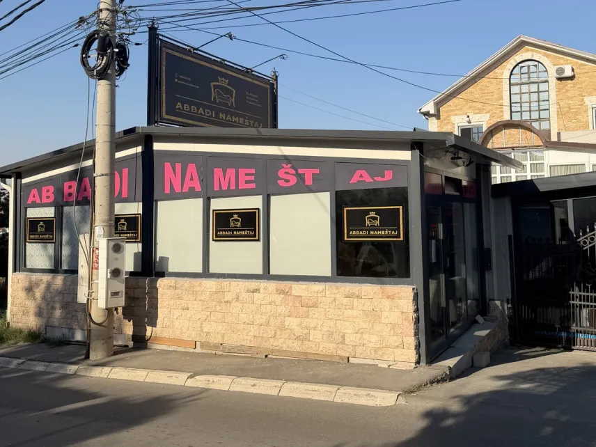 Salon ABBADI spolja — ugaona prizemna zgrada sa staklenim izlogom, natpisom ABBADI NAMEŠTAJ preko izloga i osvetljenom tablom na krovu, na uglu ulice u Beogradu.