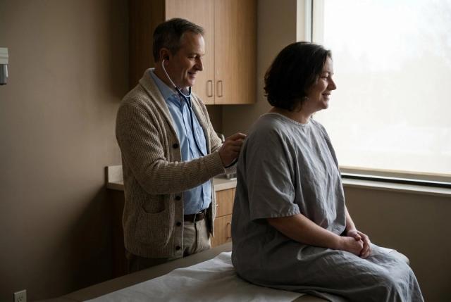 A doctor examining a patient's chest with a stethoscope in a clinic exam room.