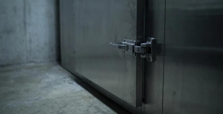 A closed, locked stainless steel mortuary door in dim light, representing a funeral home's duty to protect those in its care.