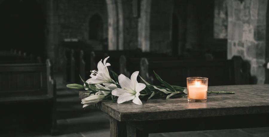 White lilies and a lit memorial candle in a softly lit chapel, representing a dignified burial or cremation.