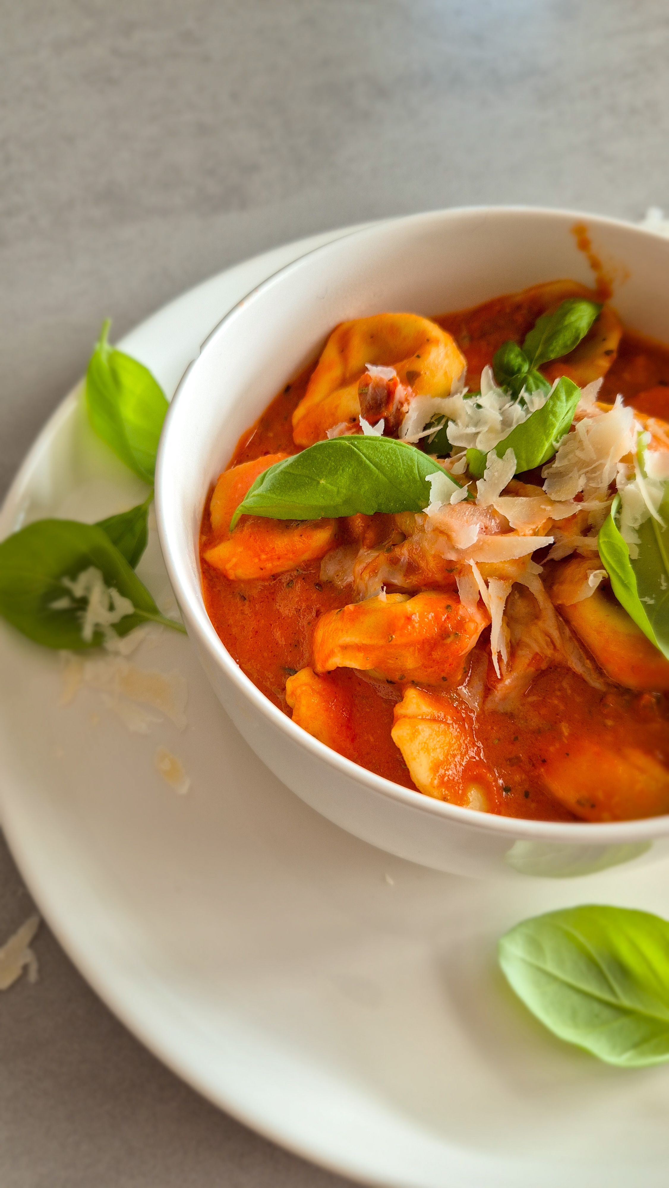 Cremige One Pot Tortellini in Tomaten-Sahne-Sauce in einer schlichten weißen Schale serviert und mit Basilikum und Parmesan garniert.