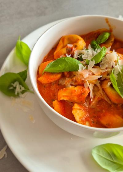 Cremige One Pot Tortellini in Tomaten-Sahne-Sauce in einer schlichten weißen Schale serviert und mit Basilikum und Parmesan garniert.
