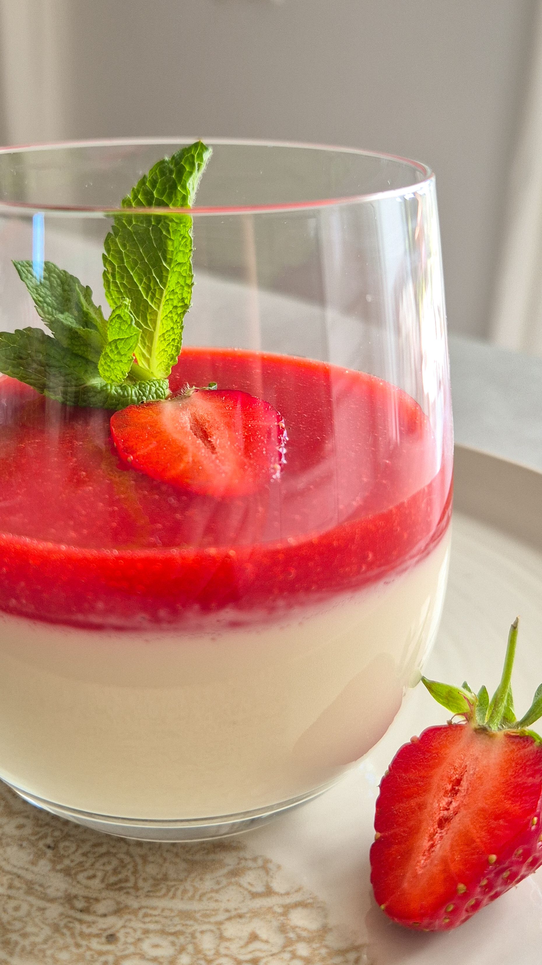 Ein Dessert-Glas cremige Panna Cotta mit frischer Erdbeersauce, Erdbeeren und Minze.
