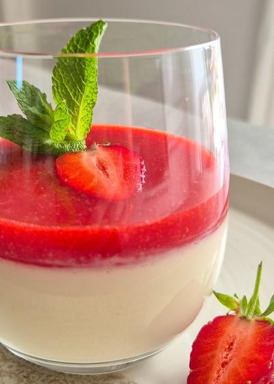 Ein Dessert-Glas cremige Panna Cotta mit frischer Erdbeersauce, Erdbeeren und Minze.