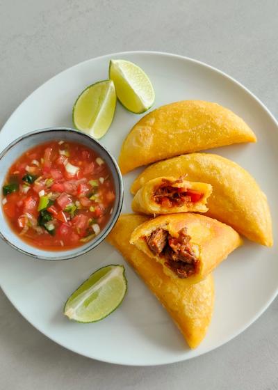 knusprige Empanadas aus P.A.N Maismehl mit Carne Mechada Füllung und Ají casero auf einem Teller.
