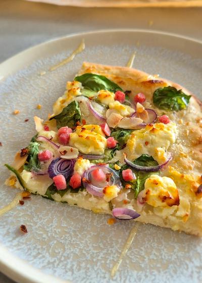 Ein Stück Flammenkuchen mit Spinat, Feta und Zwiebeln frisch aus dem Ofen.