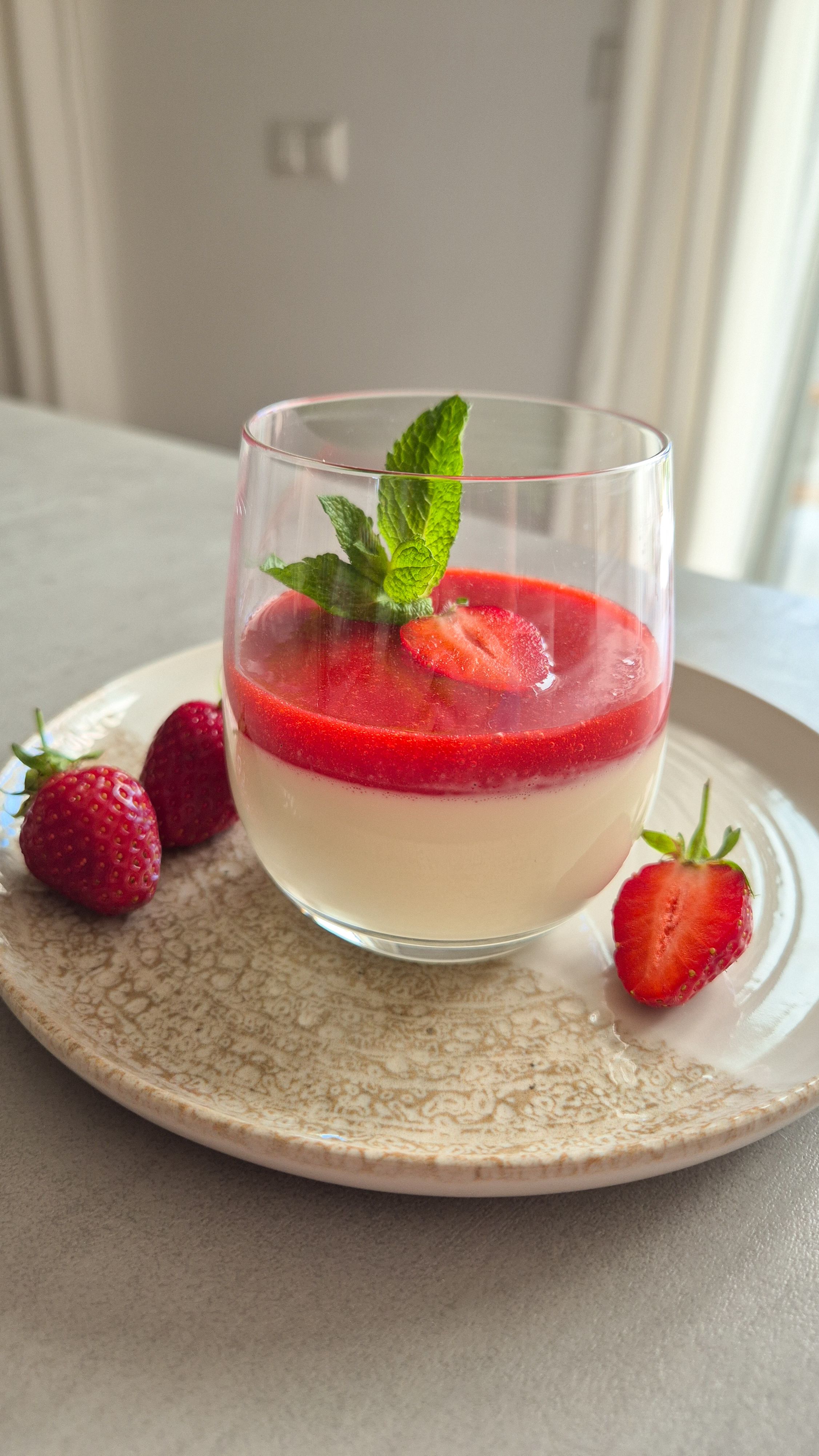 Ein Dessert-Glas cremige Panna Cotta mit frischer Erdbeersauce, Erdbeeren und Minze.