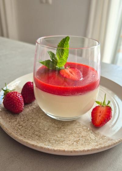 Ein Dessert-Glas cremige Panna Cotta mit frischer Erdbeersauce, Erdbeeren und Minze.