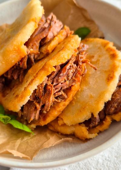 Venezolanische Arepas aus P.A.N. Maismehl mit Carne Mechada auf einem Teller.