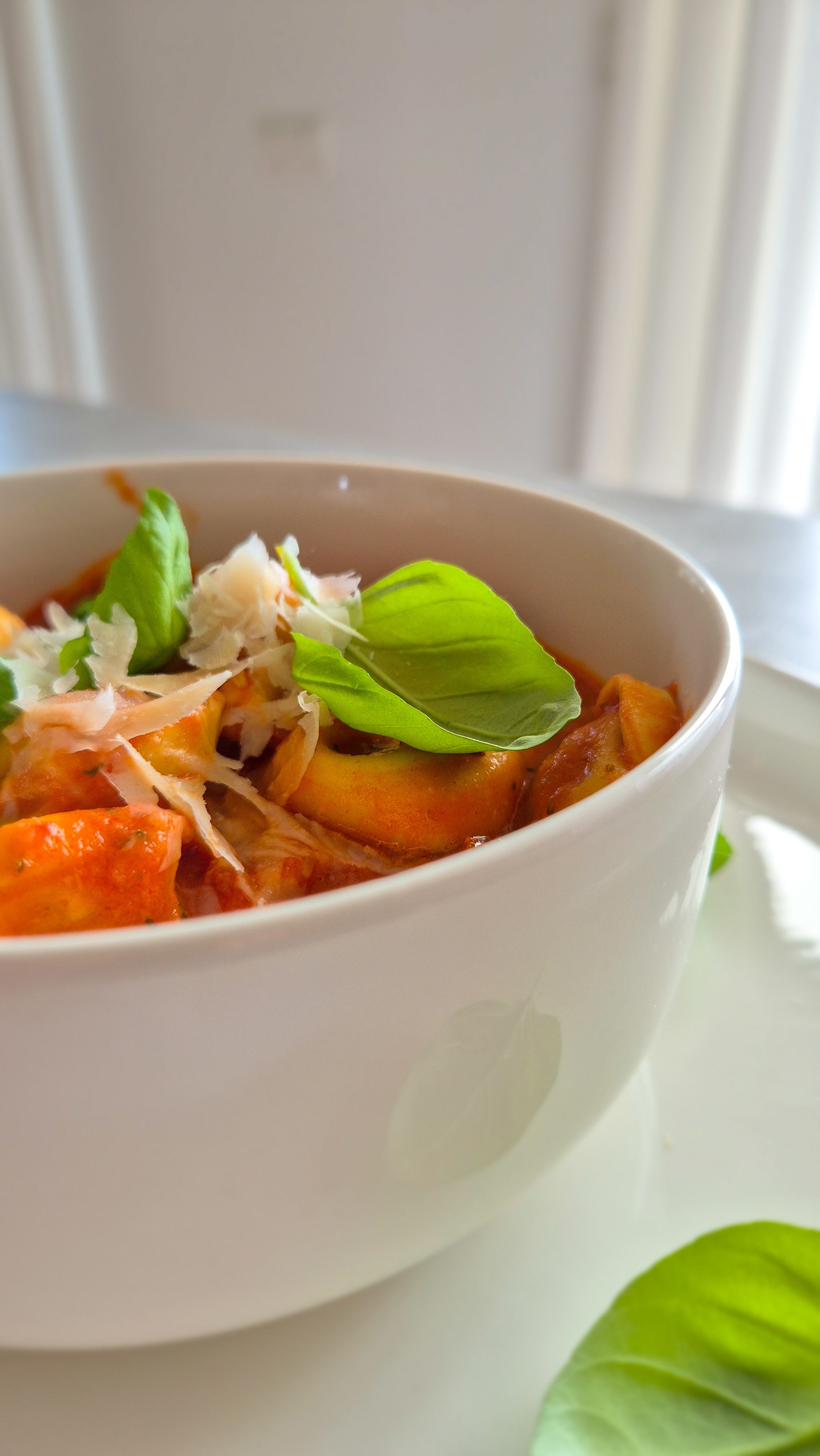 Cremige One Pot Tortellini in Tomaten-Sahne-Sauce in einer schlichten weißen Schale serviert und mit Basilikum und Parmesan garniert.