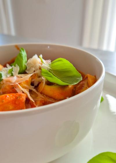 Cremige One Pot Tortellini in Tomaten-Sahne-Sauce in einer schlichten weißen Schale serviert und mit Basilikum und Parmesan garniert.