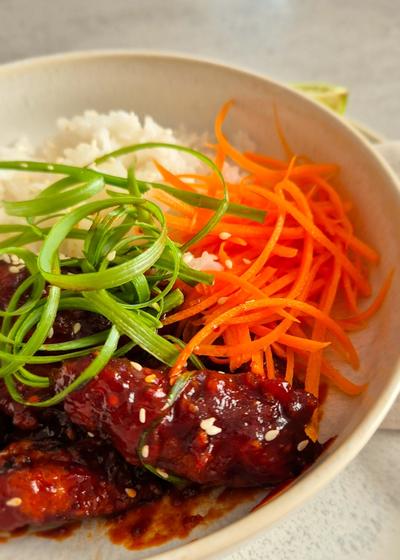 Koreanisches Fried Chicken - Yangnyeom - mit Frühlingszwiebeln und Sesam zu Reis und Karotten in einer Schale serviert.