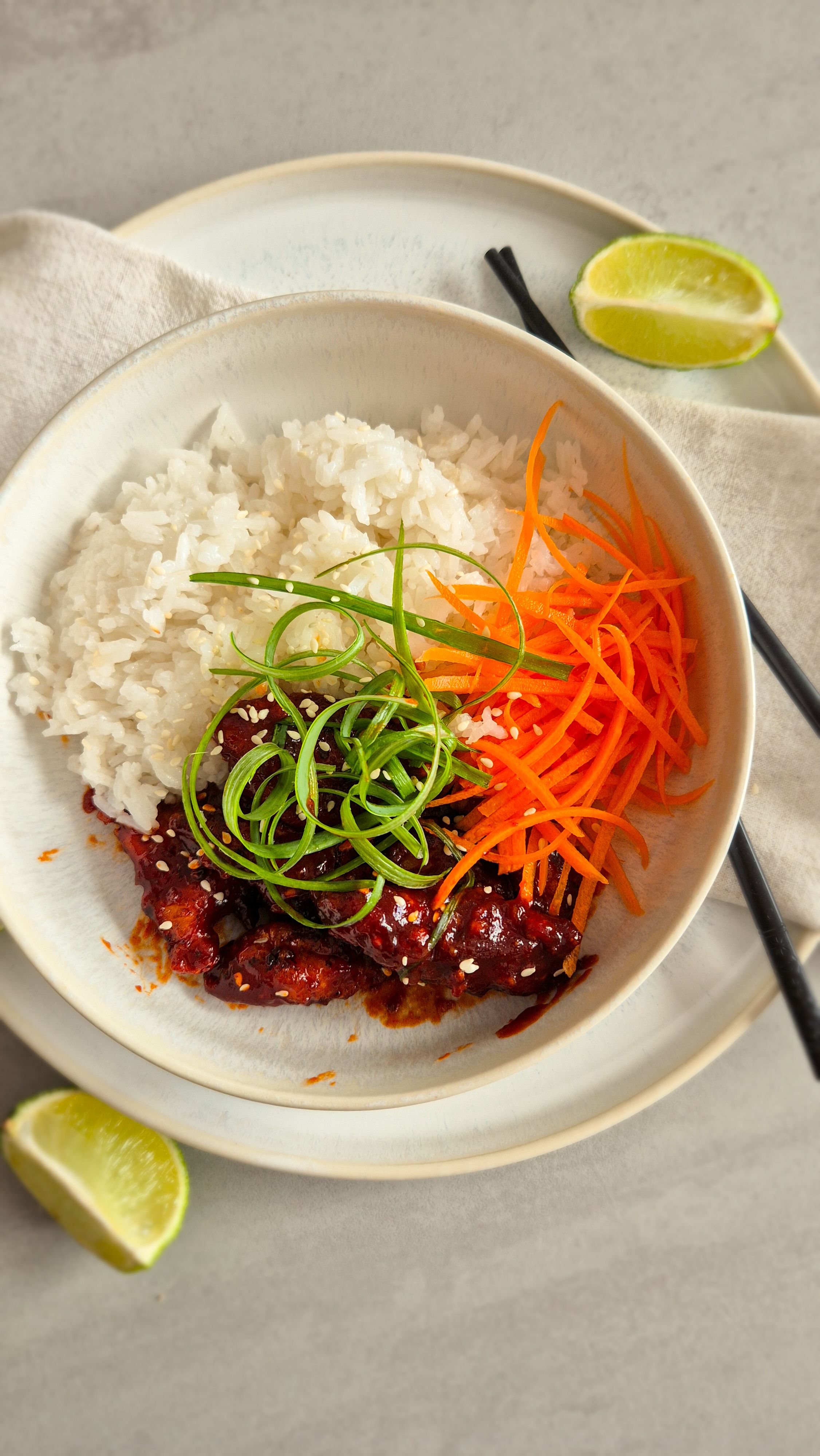 Koreanisches Fried Chicken - Yangnyeom - mit Frühlingszwiebeln und Sesam zu Reis und Karotten in einer Schale serviert.