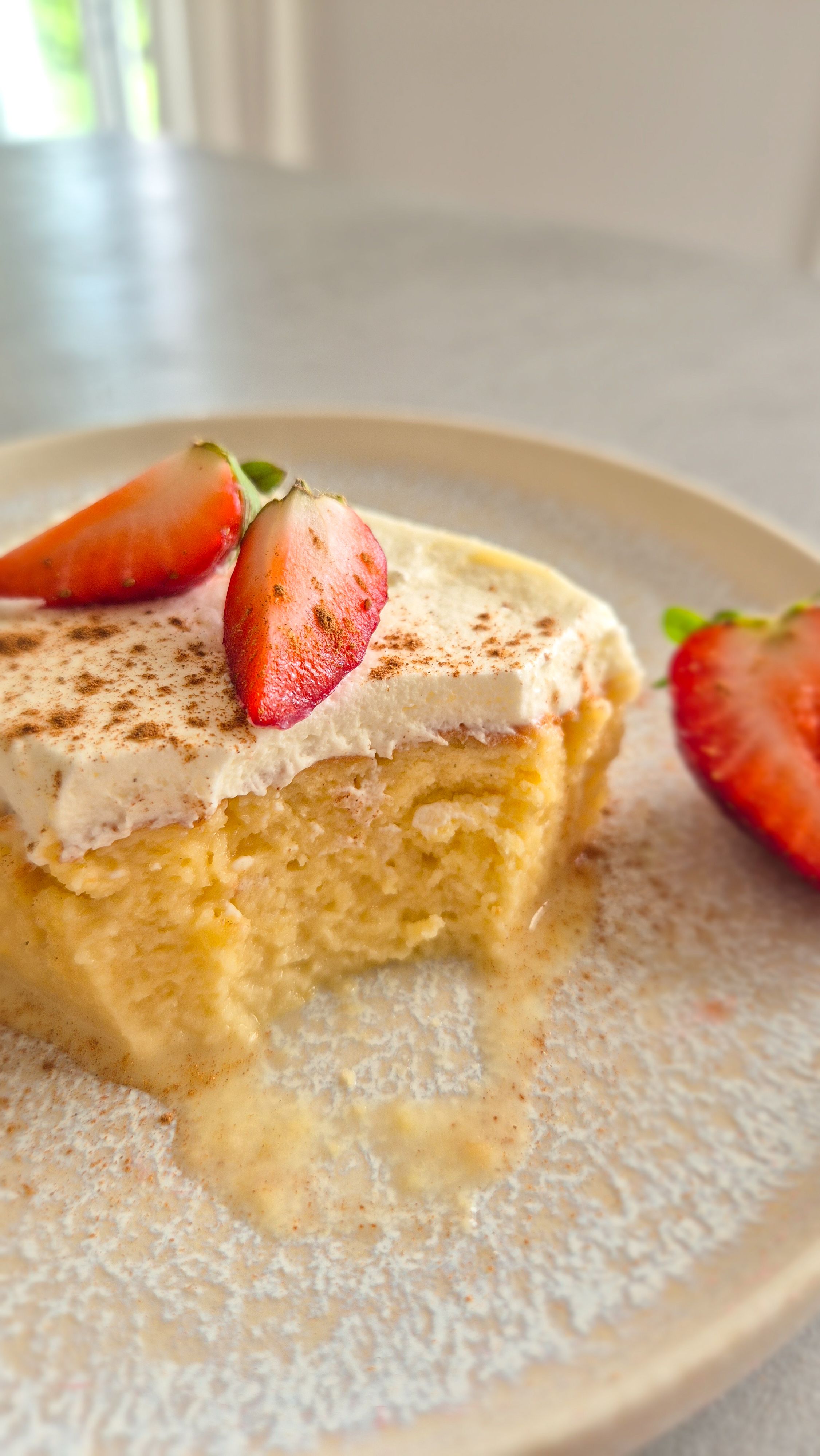 Ein Stück saftiger Tres Leches Kuchen (3 Milch Kuchen) aus Lateinamerika mit einer Sahnehaube und frischen Erdbeeren auf einem Teller serviert.