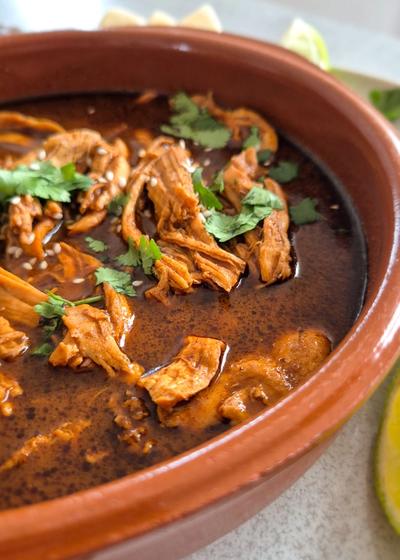 Mole Poblano wie aus Mexiko in einer Cazuela mit Koriander, Sesam und Avocado seerviert.