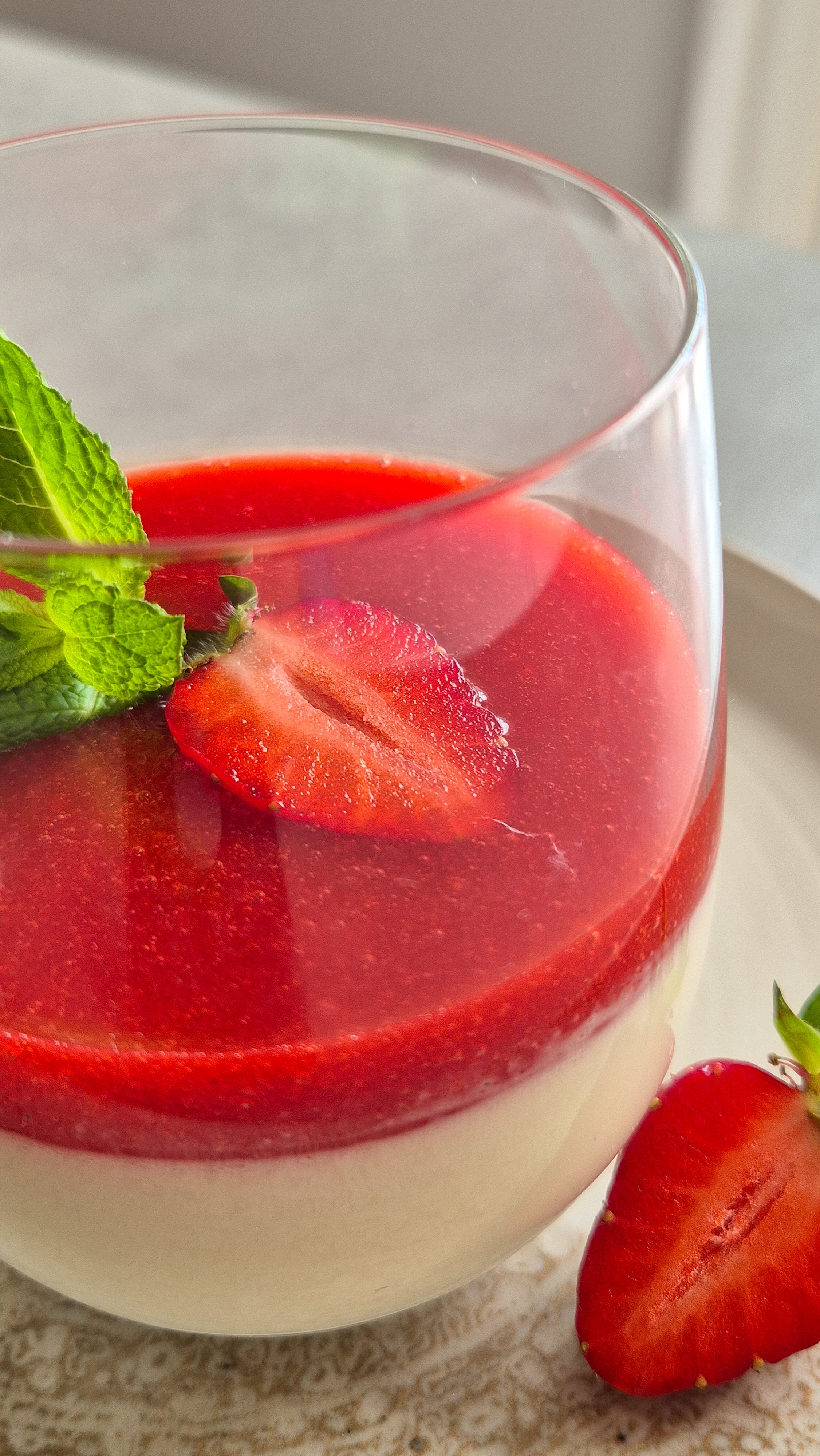 Cremige Panna Cotte mit frischer Erdbeersauce im Glas. Mit einer Erdbeere und Minze serviert.
