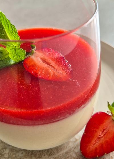 Cremige Panna Cotte mit frischer Erdbeersauce im Glas. Mit einer Erdbeere und Minze serviert.