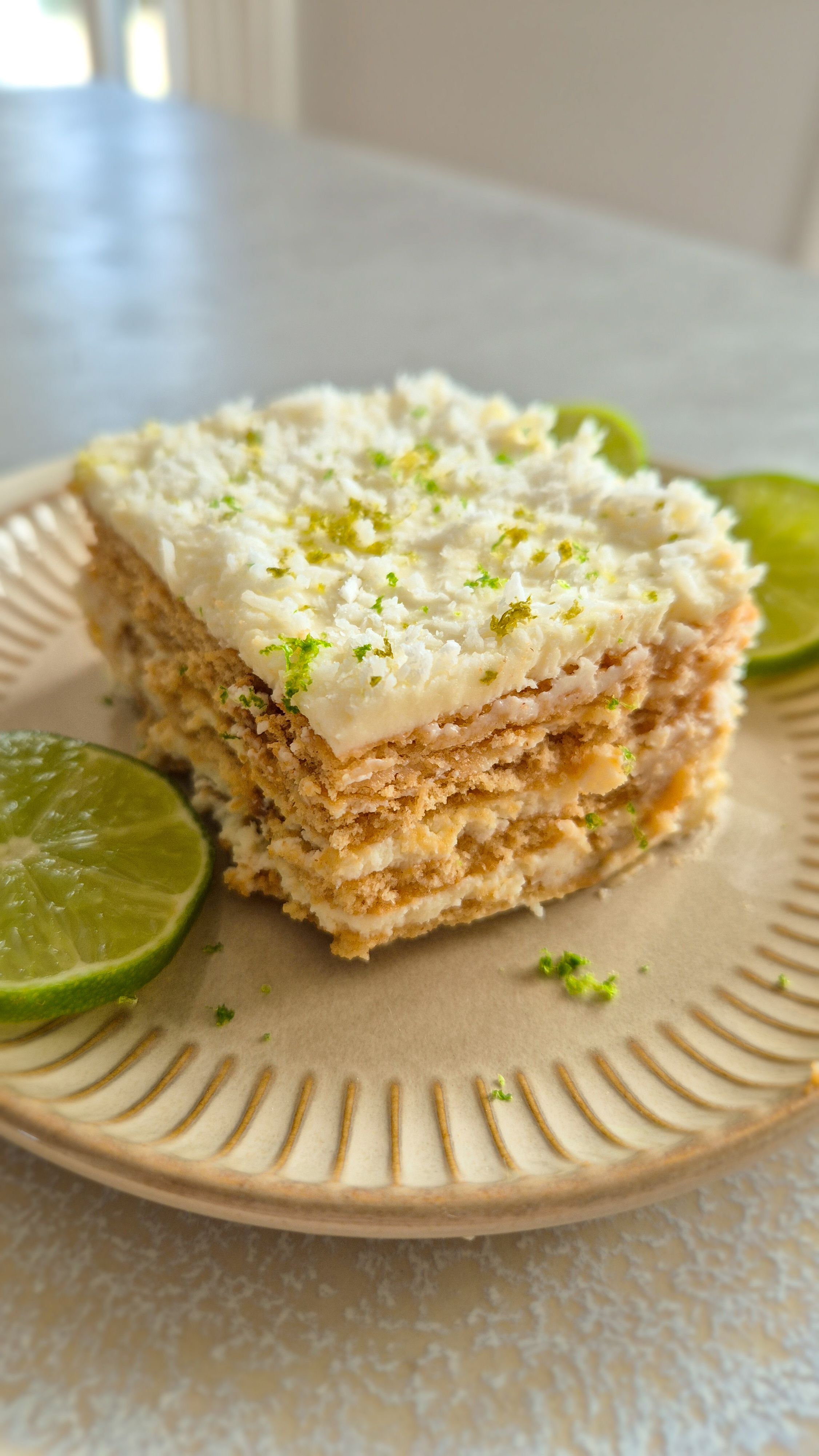 Ein Stück Carlota de Limón (mexikanischer Limettenkuchen) auf einem beigen Teller mit Limettenscheiben serviert. 