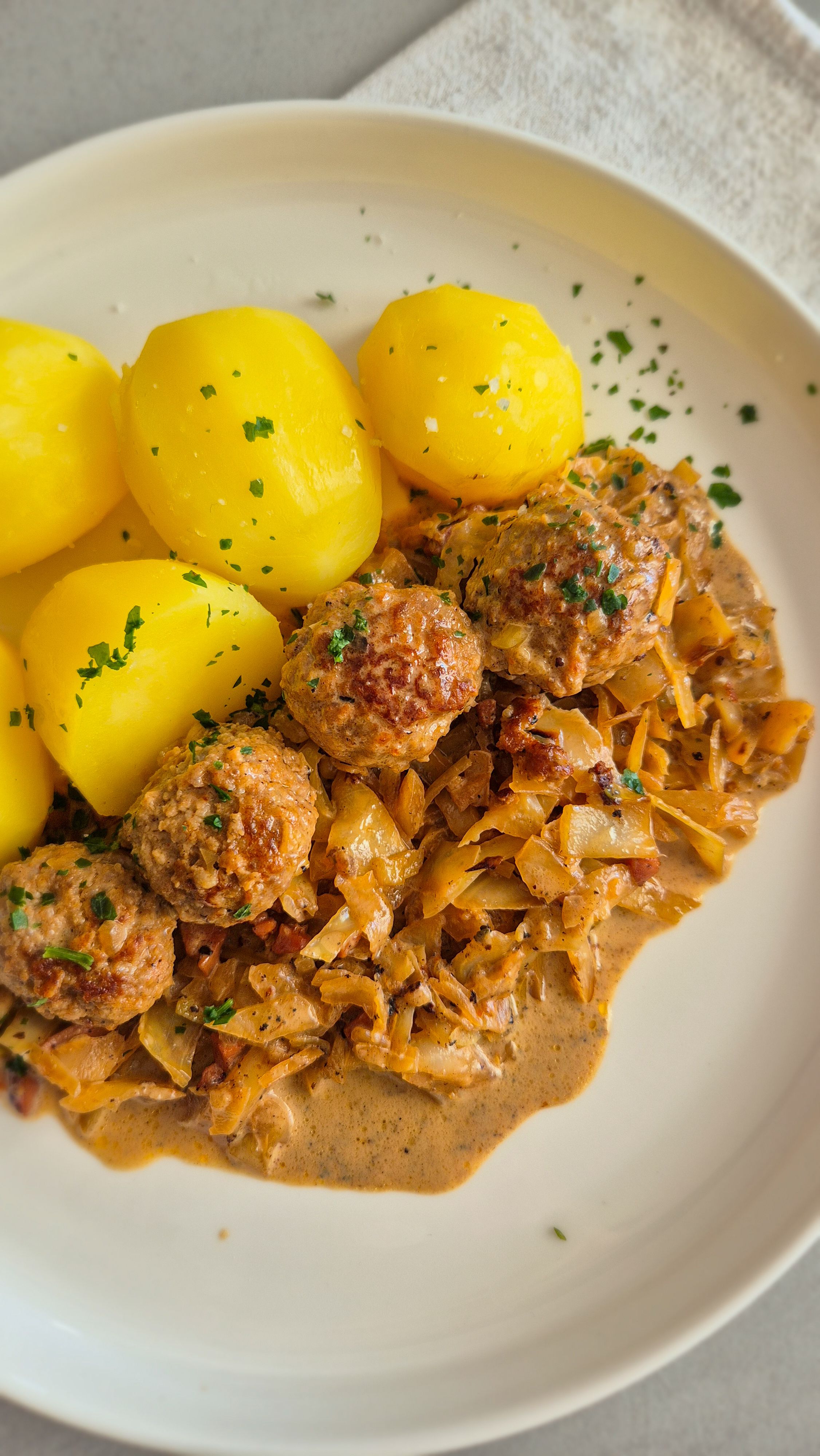 Hackbällchen mit gedünstetem Weißkohl in cremiger Sauce und Salzkartoffeln auf einem Teller.