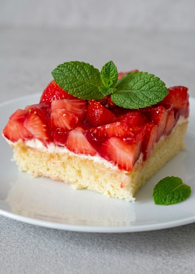 Ein Stück Erdbeerkuchen mit Mascarpone-Creme und Minze auf einem Teller.