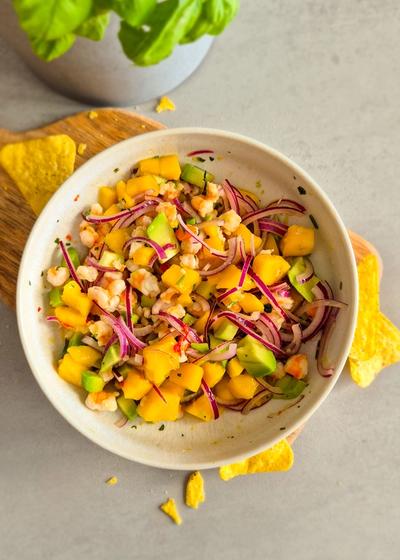 Servierfertiges Garnelen Ceviche mit Mango und Avocado in einer beigen Schale mit Tortilla-Chips