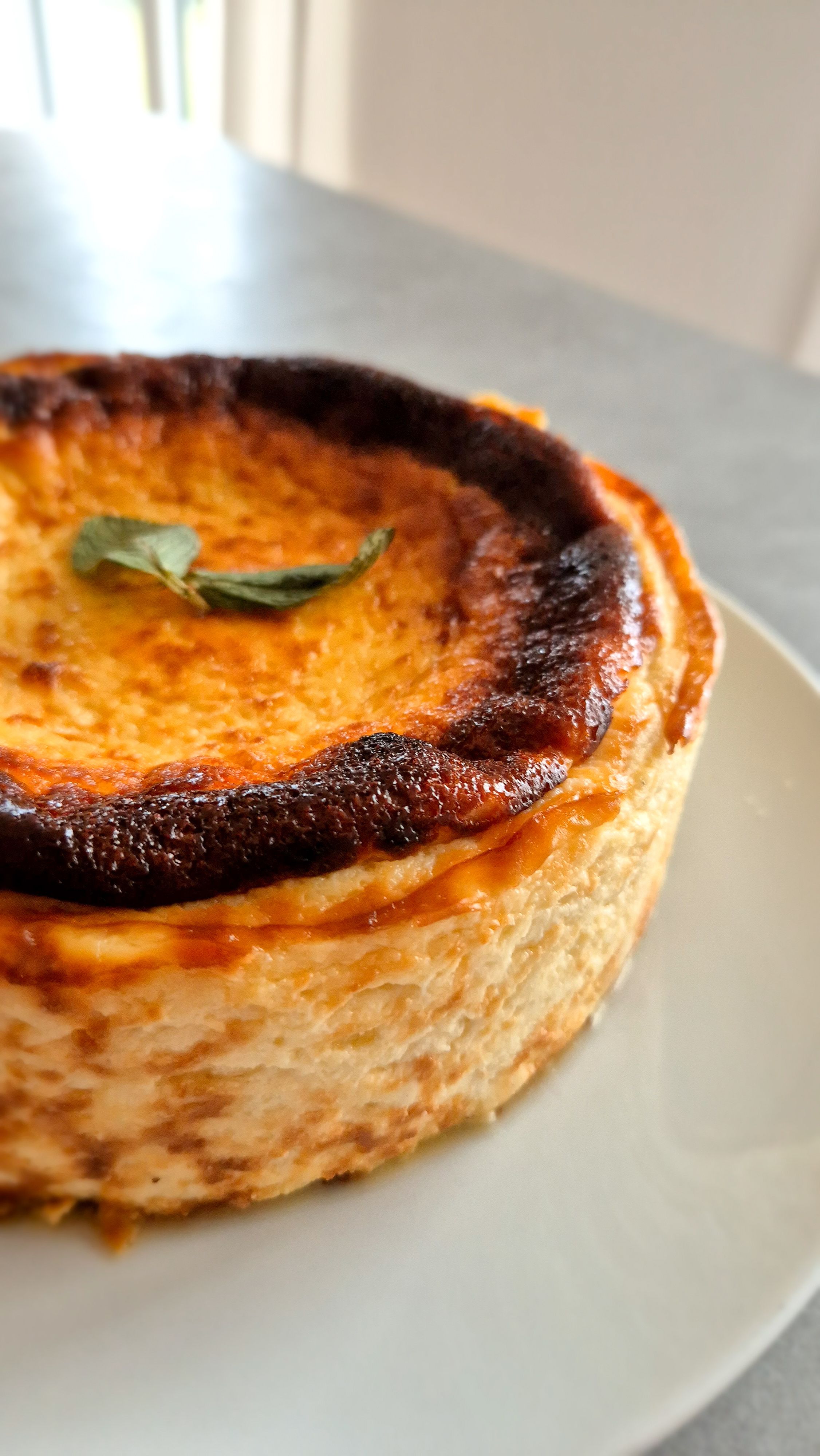 Rustikaler San Sebastian Cheesecake mit einer dunkelbraun karamellisierten Kruste und cremigen Kern auf einem Teller.