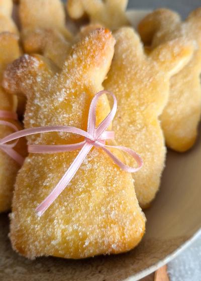 Ein paar Quarkhasen aus Quark-Öl-Teig auf einem rustikalen Teller neben pinken Tulpen zu Ostern.