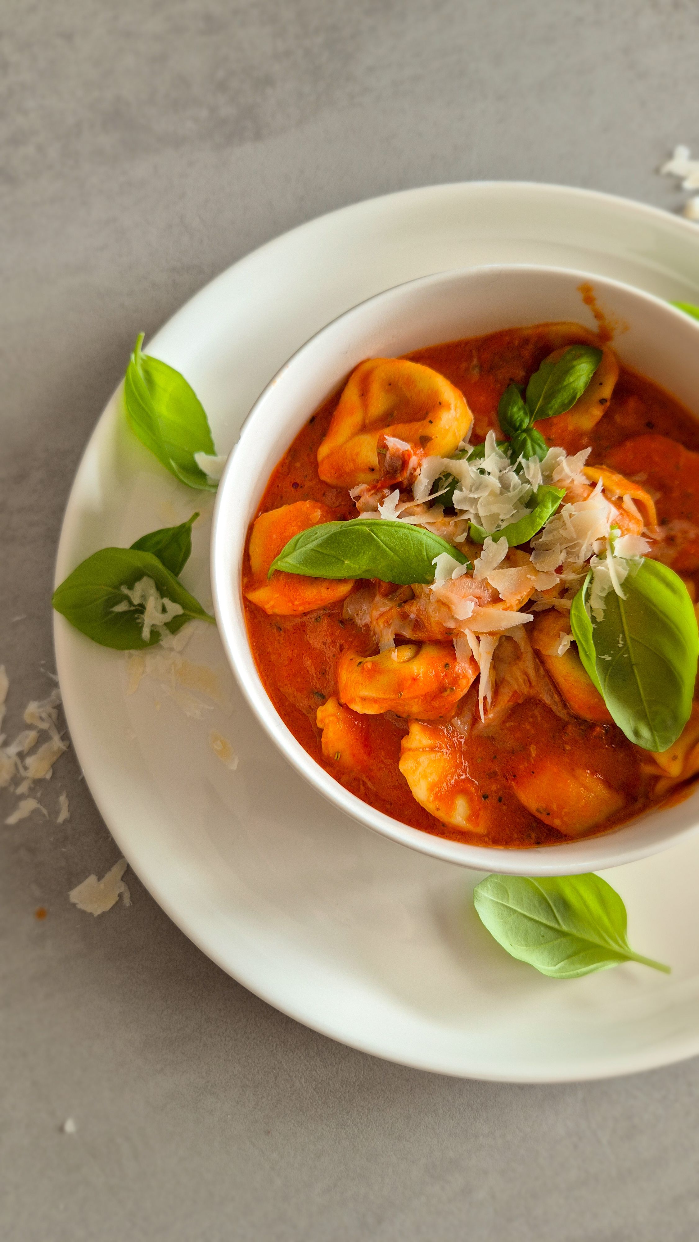 Cremige One Pot Tortellini in Tomaten-Sahne-Sauce in einer schlichten weißen Schale serviert und mit Basilikum und Parmesan garniert.