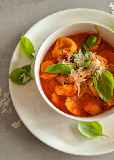 Cremige One Pot Tortellini in Tomaten-Sahne-Sauce in einer schlichten weißen Schale serviert und mit Basilikum und Parmesan garniert.