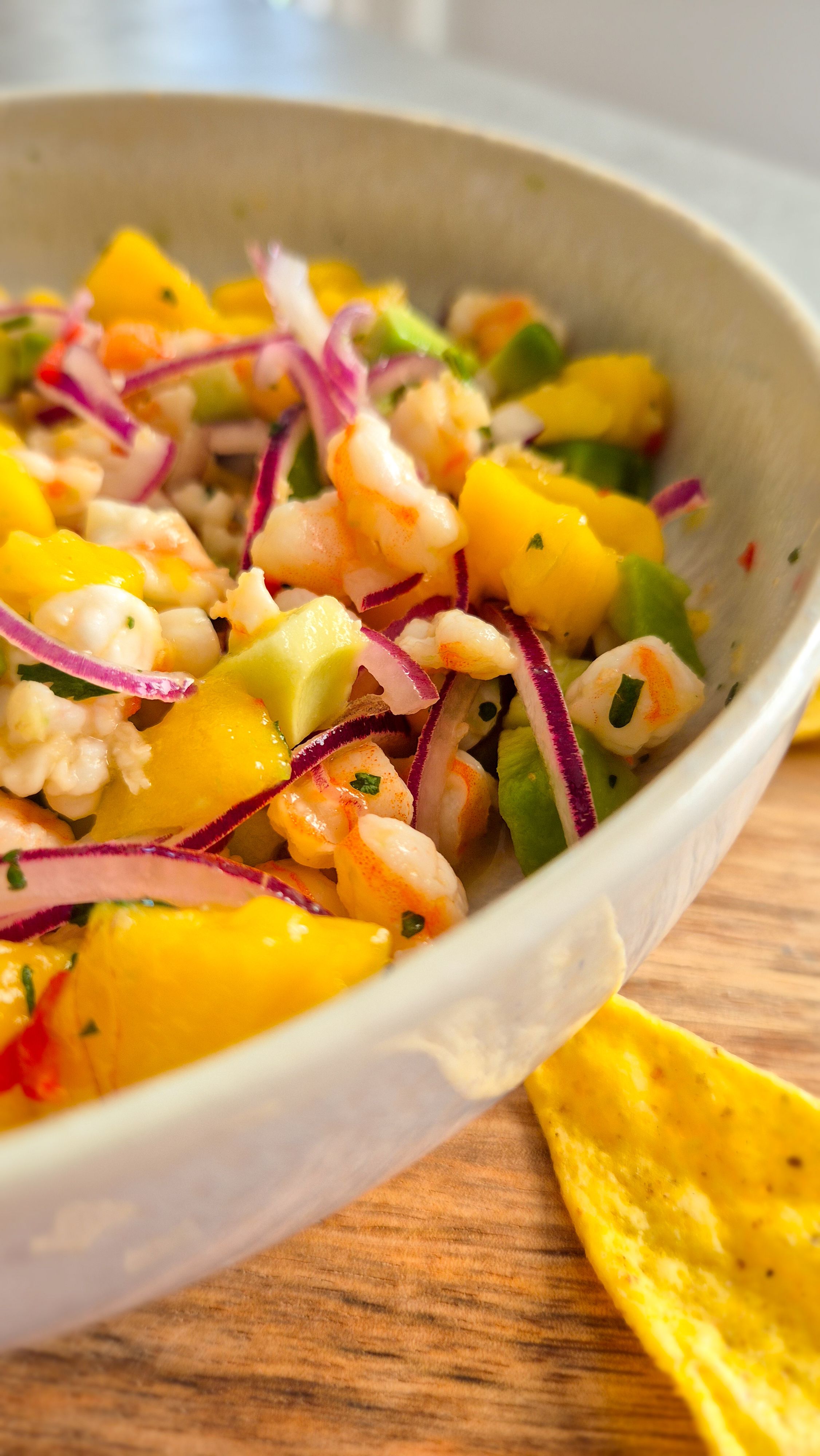 Servierfertiges Garnelen Ceviche mit Mango und Avocado in einer beigen Schale mit Tortilla-Chips