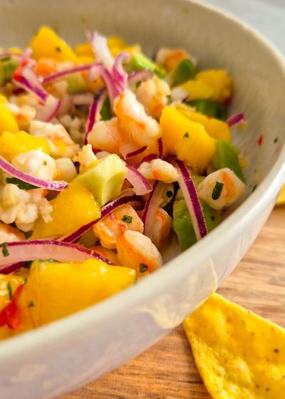 Servierfertiges Garnelen Ceviche mit Mango und Avocado in einer beigen Schale mit Tortilla-Chips
