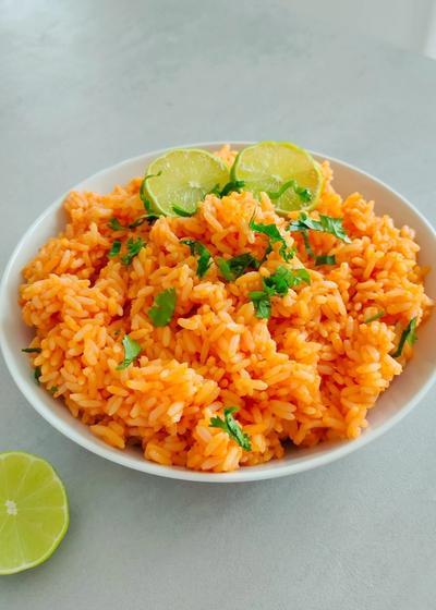 Mexikanischer Reis - Arroz Rojo - auf einem Teller mit Koriander garniert und Limetten serviert.