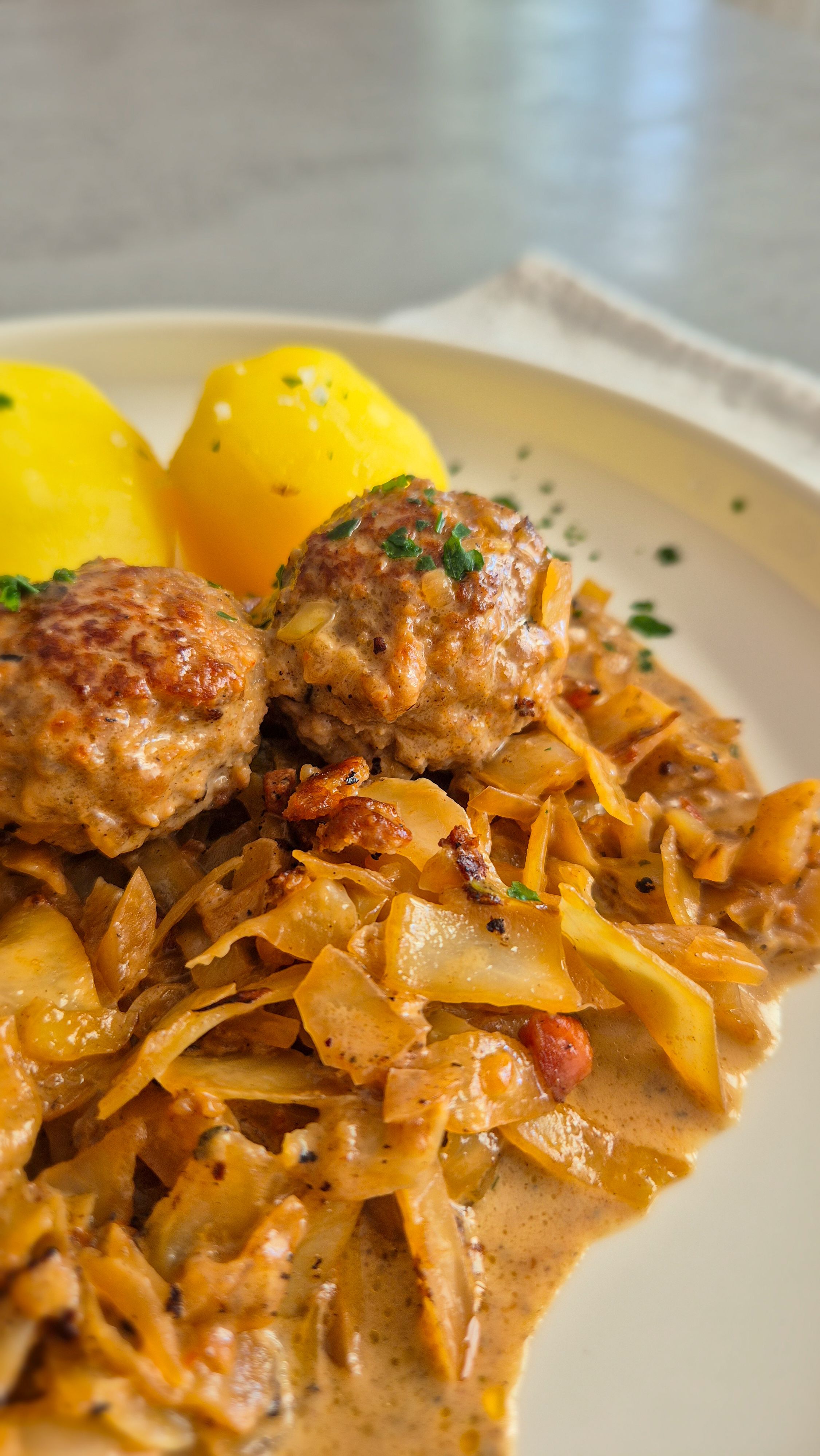 Hackbällchen mit gedünstetem Weißkohl in cremiger Sauce und Salzkartoffeln auf einem Teller.