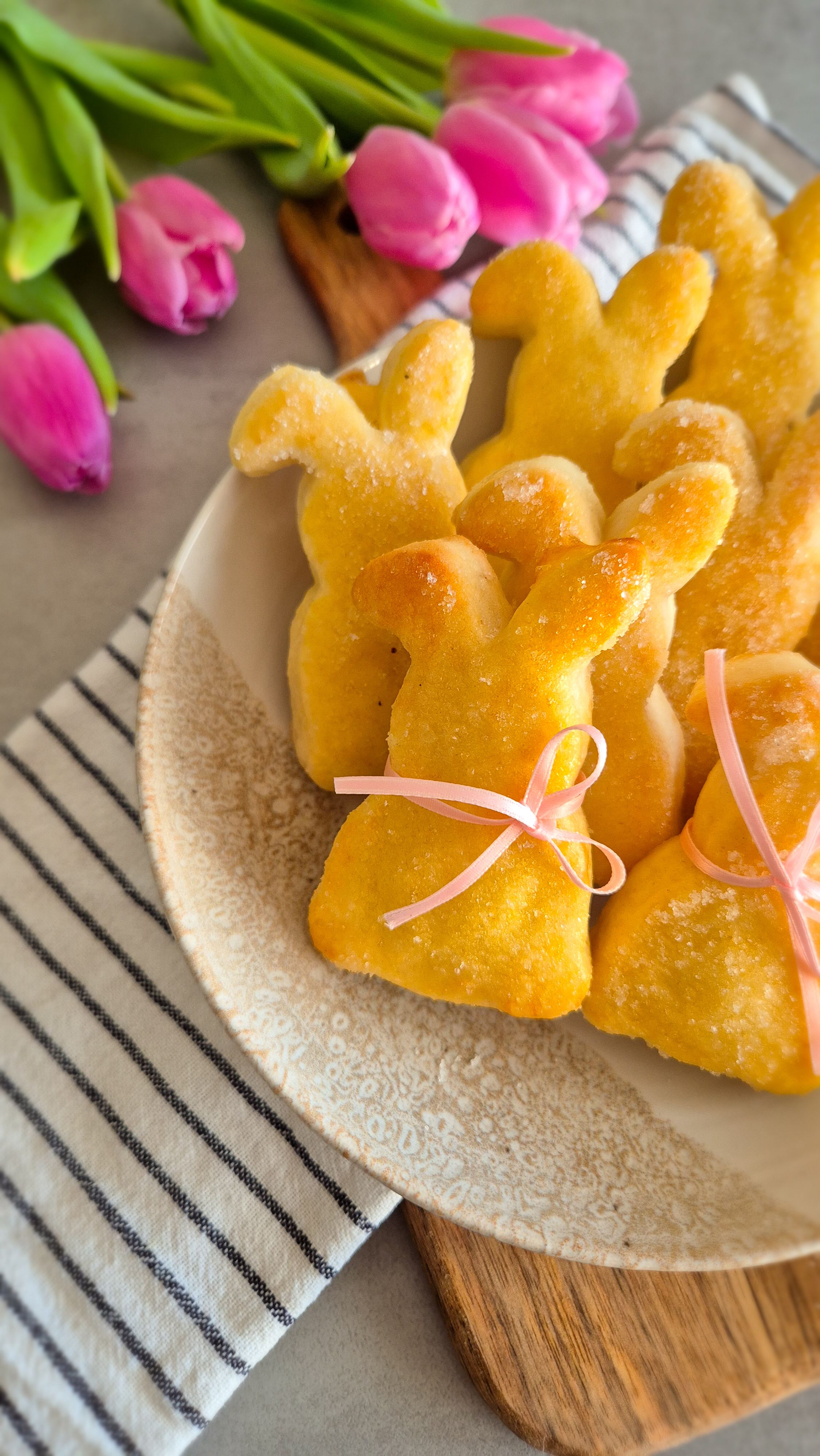 Ein paar Quarkhasen aus Quark-Öl-Teig auf einem rustikalen Teller neben pinken Tulpen zu Ostern.