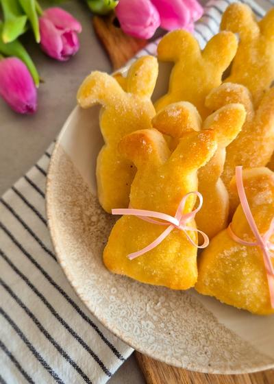 Ein paar Quarkhasen aus Quark-Öl-Teig auf einem rustikalen Teller neben pinken Tulpen zu Ostern.