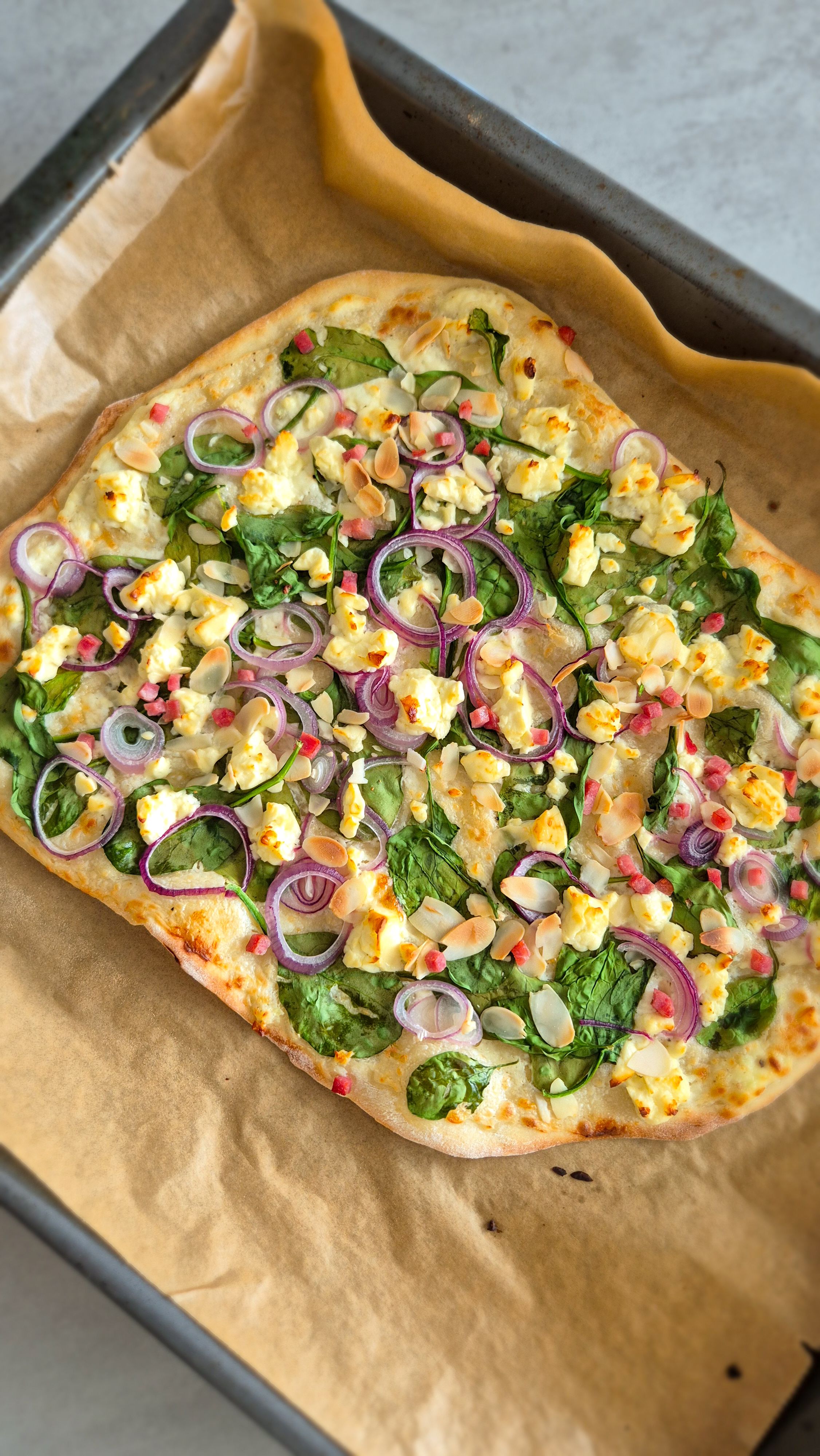 Vegetarischer Flammkuchen mit Spinat auf einem Backblech. 