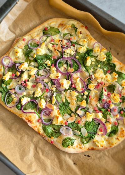 Vegetarischer Flammkuchen mit Spinat auf einem Backblech.