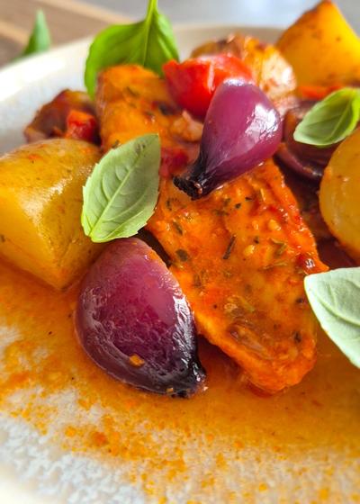 Einfaches Blechgericht mit Hähnchenbrust, Kartoffeln und Tomaten auf einem Teller serviert.