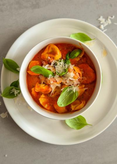 Cremige One Pot Tortellini in Tomaten-Sahne-Sauce in einer schlichten weißen Schale serviert.