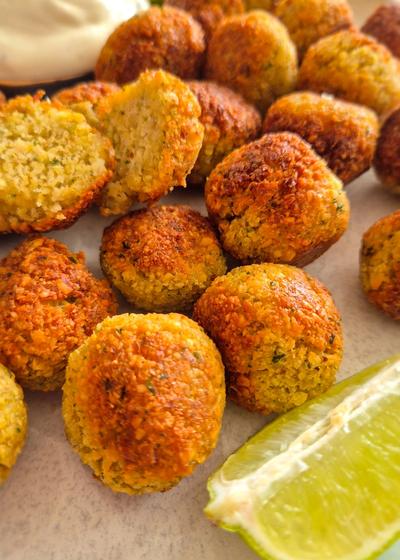 Ein rustikaler Teller mit knusprigen Falafel mit Limetten-Scheiben und Tzatziki.
