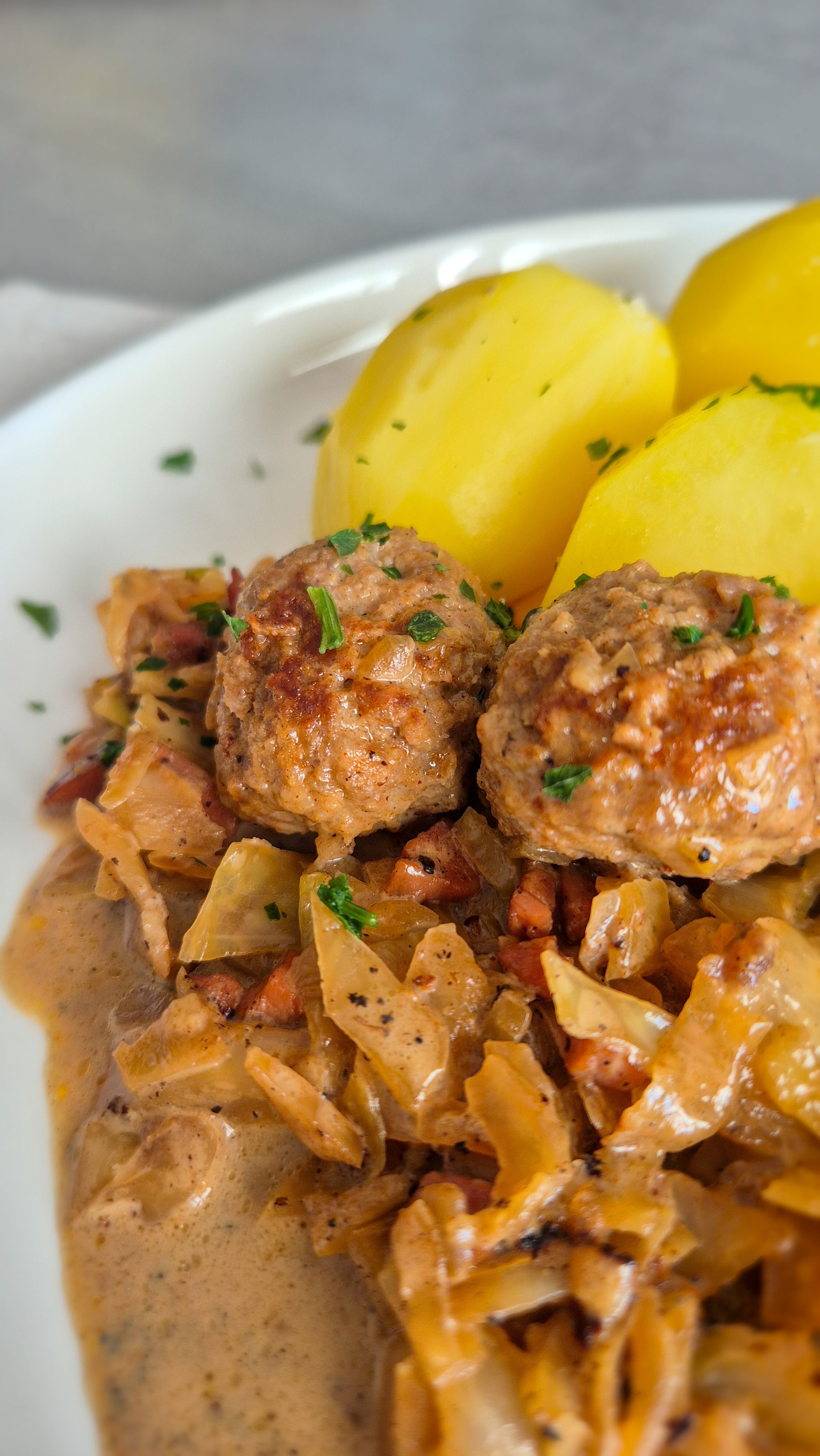 Hackbällchen mit gedünstetem Weißkohl in cremiger Sauce und Salzkartoffeln auf einem Teller.