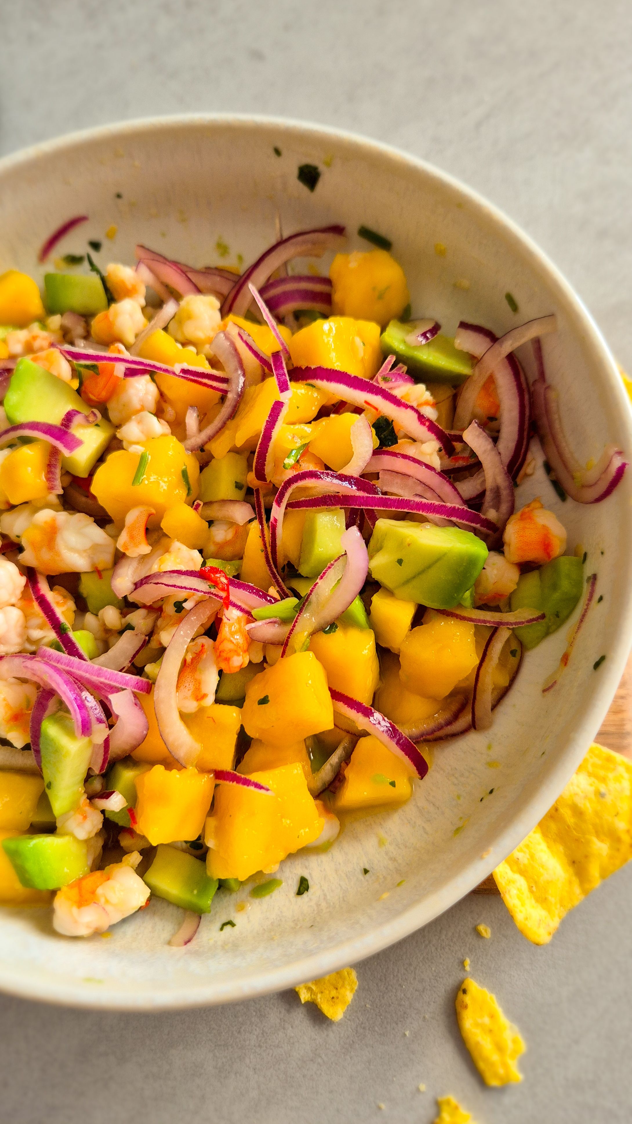 Servierfertiges Garnelen Ceviche mit Mango und Avocado in einer beigen Schale mit Nachos Totopos