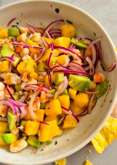 Servierfertiges Garnelen Ceviche mit Mango und Avocado in einer beigen Schale mit Nachos Totopos