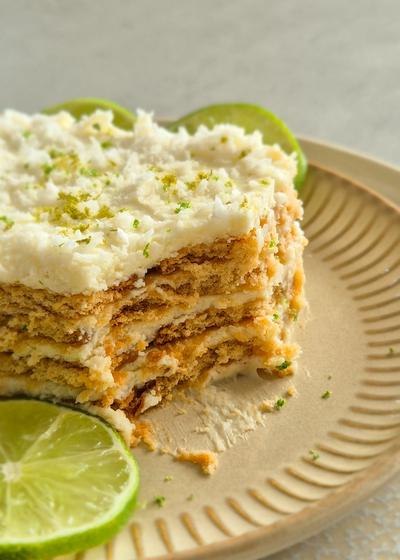 Ein Stück Carlota de Limón (mexikanischer Limettenkuchen) auf einem beigen Teller mit Limettenscheiben serviert.