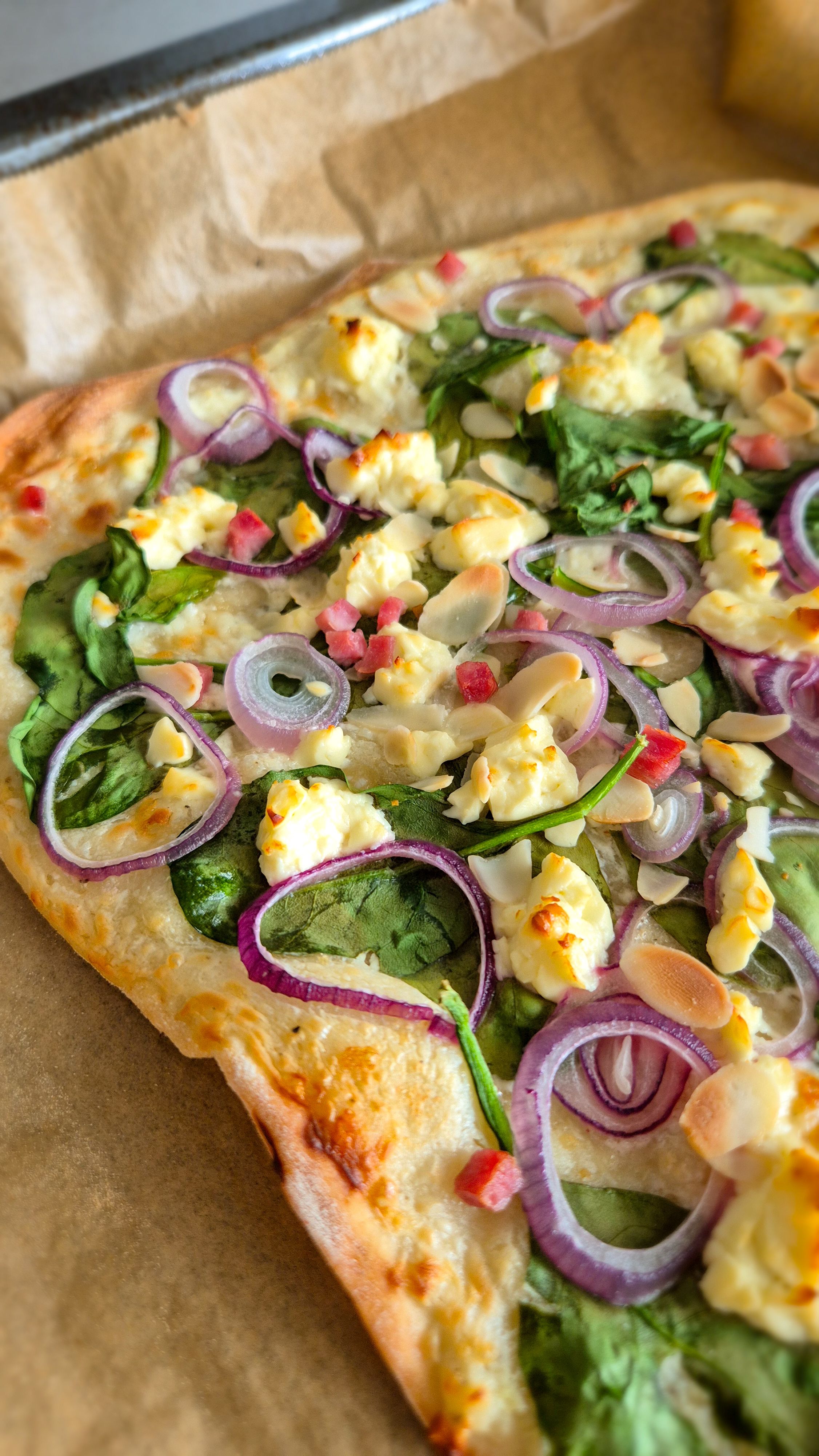 Frischer vegetarischer Flammkuchen aus dem Ofen mit Spinat, Zwiebelringen, Feta und Mandeln.