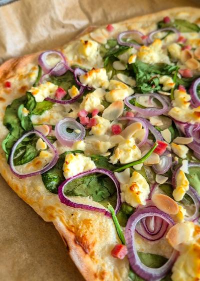 Frischer vegetarischer Flammkuchen aus dem Ofen mit Spinat, Zwiebelringen, Feta und Mandeln.