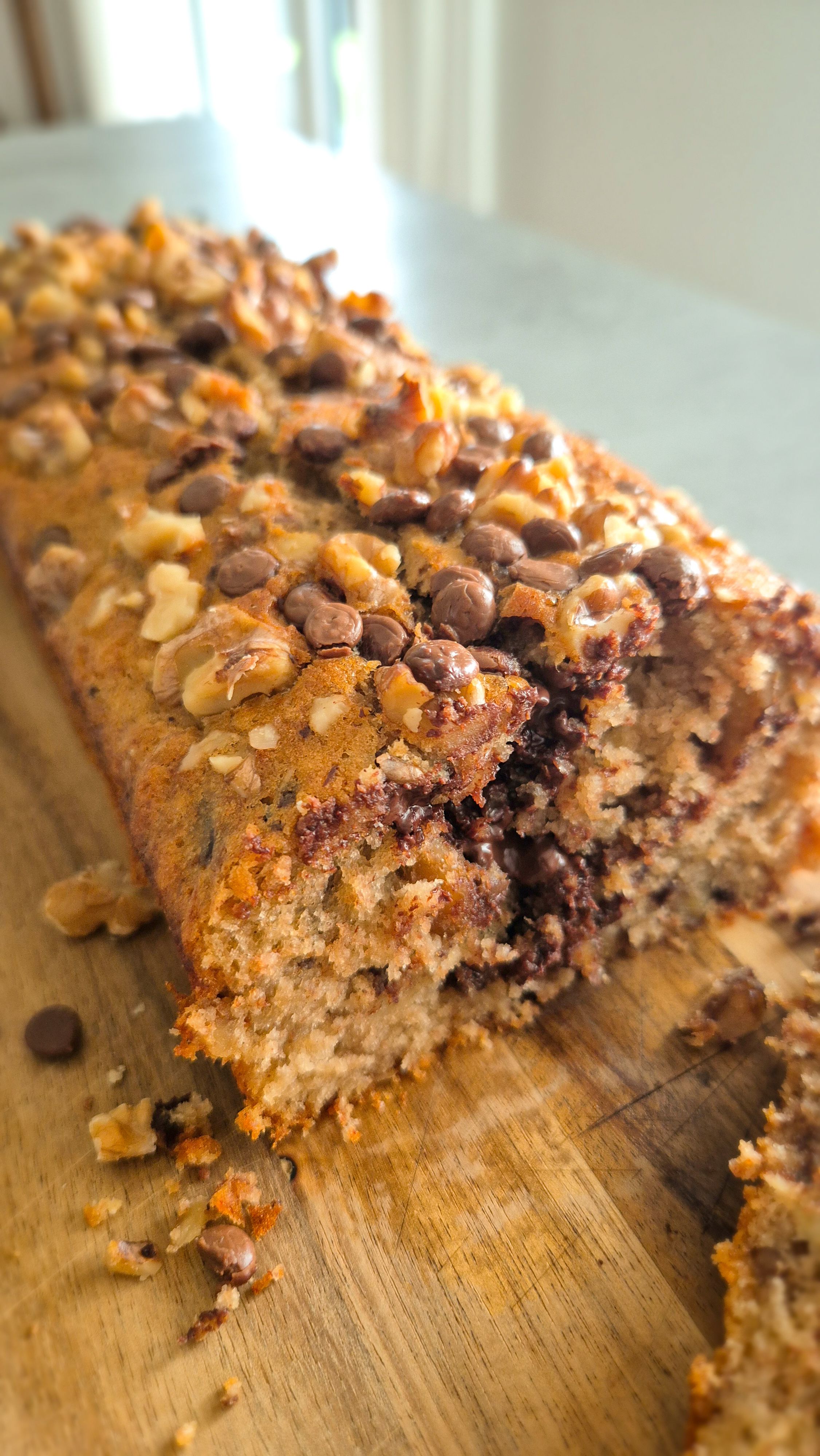 Frisch gebackenes Chunky Monkey Bananenbrot mit Walnüssen und Schokoladen-Chunks auf einem Holzbrett.