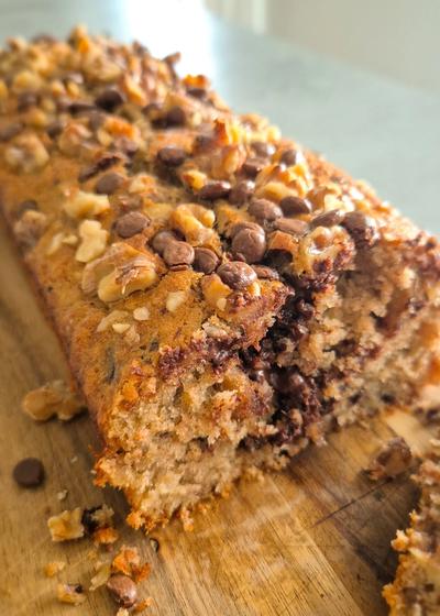 Frisch gebackenes Chunky Monkey Bananenbrot mit Walnüssen und Schokoladen-Chunks auf einem Holzbrett.