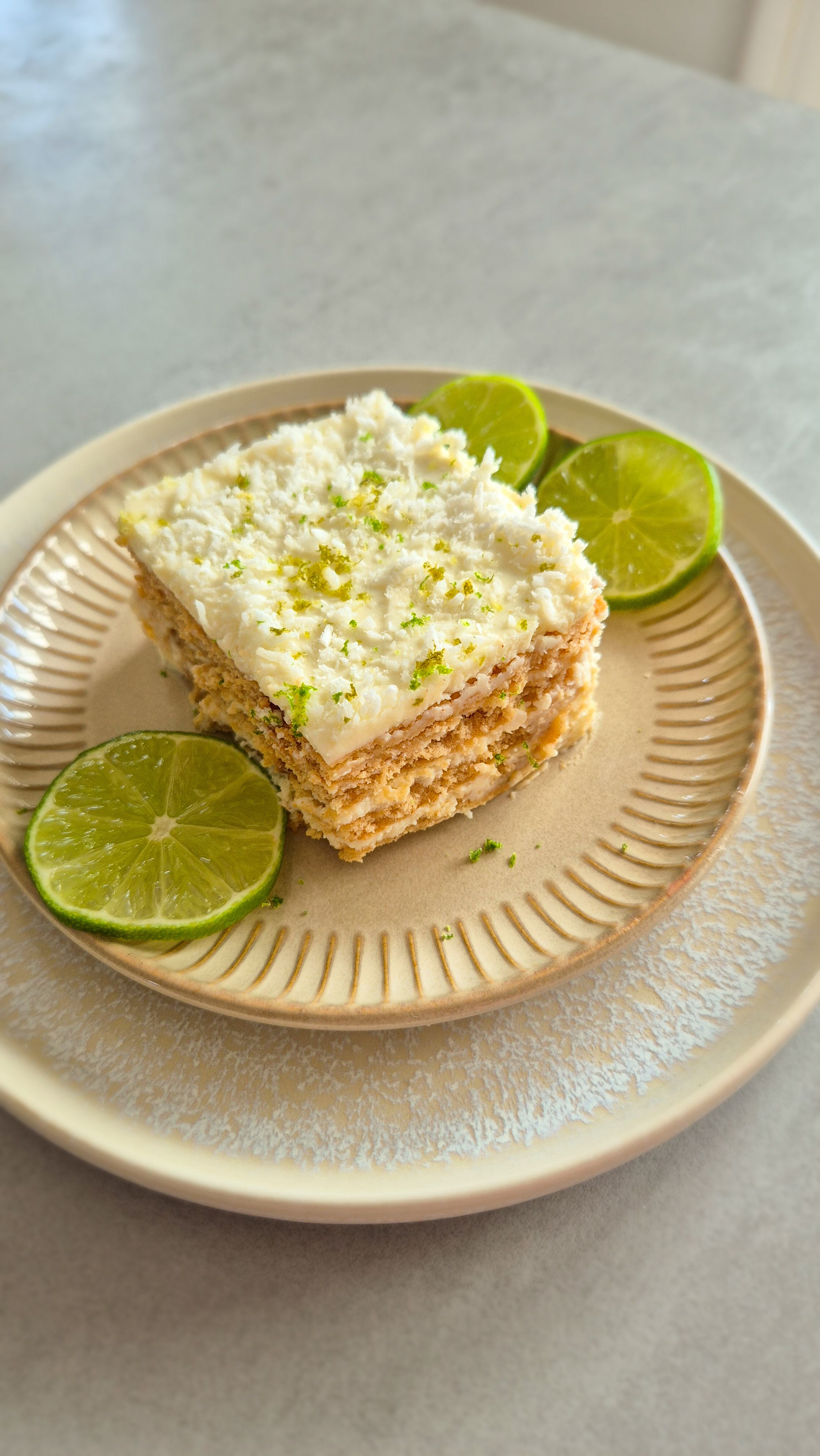 Ein Stück Carlota de Limón (mexikanischer Limettenkuchen) auf einem beigen Teller mit Limettenscheiben serviert. 